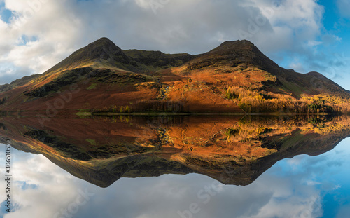 Majestic vibrant Autumn Fall landscape Buttermere in Lake District with beautiful early morning sunlight playing across the hills and mountains