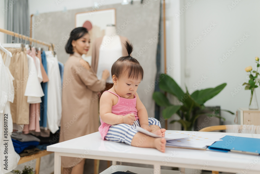 Fashion designer measuring size for tailor made while her baby sitting on table Fashion designer measuring size for tailor made while her baby sitting on table