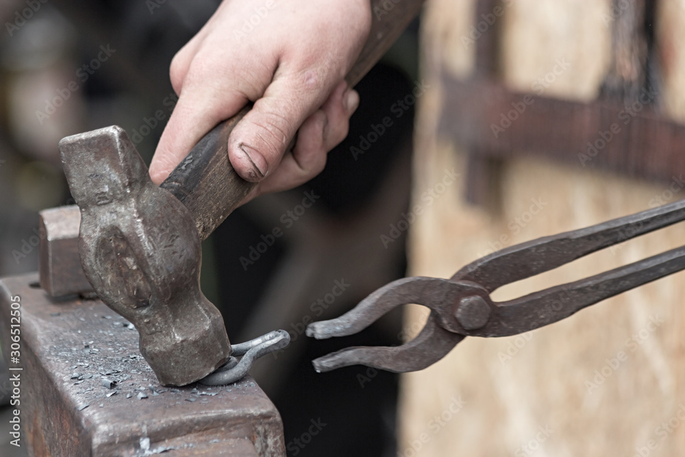 The blacksmith makes an iron loop with a hammer and tongs, forging on the anvil. The blacksmith makes an iron loop with a hammer and tongs, forging on the anvil.