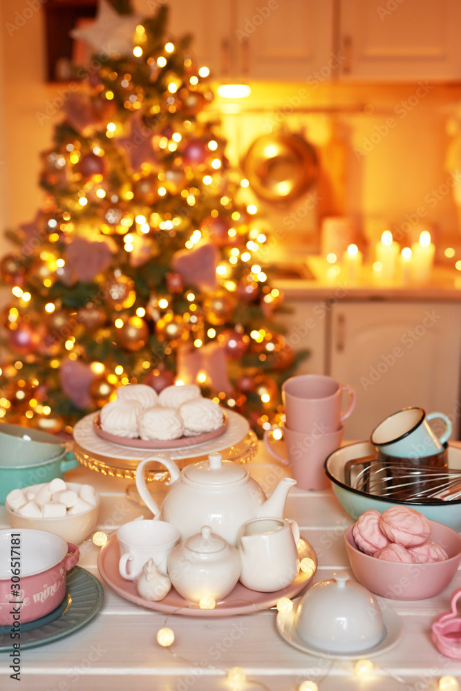 Fototapeta premium Christmas decor in kitchen. Christmas dishes and sweets. Bright interior of New Year's kitchen. New year card template. The kitchen is white and pink colors. Christmas tree in the kitchen