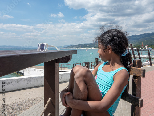 Obraz na plátně Jamaican European ethnicity little girl sitting at a empty table on the sea beac