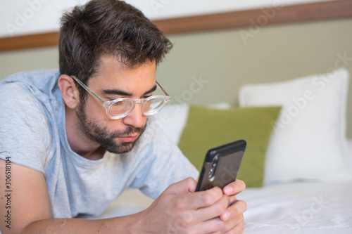 Young man typing a message in bed
