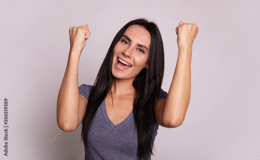 Fototapeta premium Success! Close-up photo of a good-looking excited woman with long chestnut hair, who is posing with her both hands in fists and her mouth wide open, expressing success.