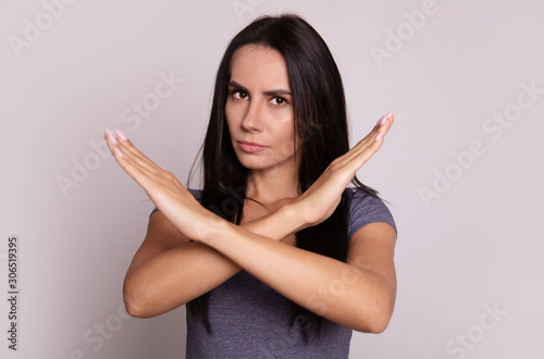 Tapeta Please, do not! Close-up photo of a young serious dark-haired girl in a grey t-shirt, who is looking in the camera and showing a cross with her arms
