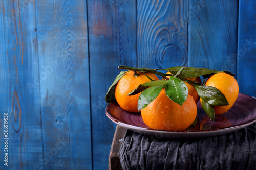 Mandarins with green leaves on the ceramic plate against the blue wooden background