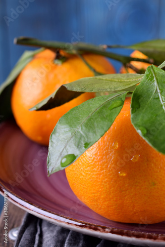 Mandarins with green leaves on the ceramic plate against the blue wooden background