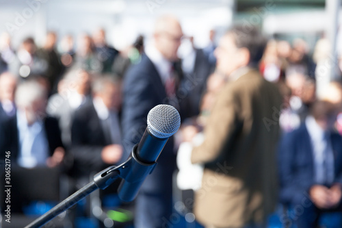 Business conference or corporate presentation. Microphone in focus against blurred audience.