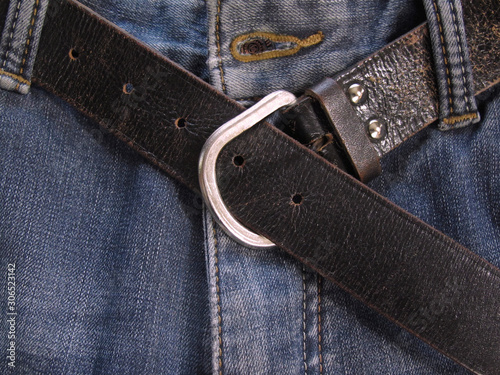Old leather belt on jeans. Vintage brown trouser belt. Blue jeans background. Men's casual closet. Denim texture.