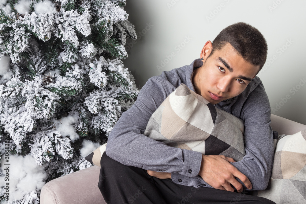 Obraz premium Young happy man sitting on couch near christmas tree