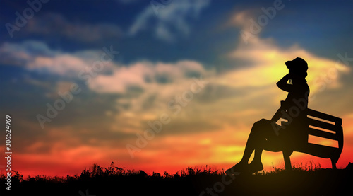The silhouette of a girl sitting on a bench watching the sunset.