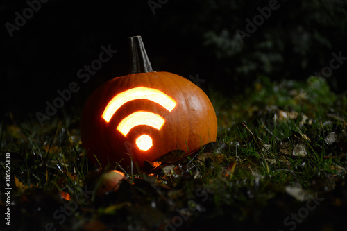 Closeup photo of pumpkin with carved Wi-Fi signal during Halloween night. Shot in garden with fallen apples, grass and leaves during autumn time. photo