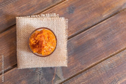 Glass bowl of homemade carrot jam with carrots and orange on concrete background