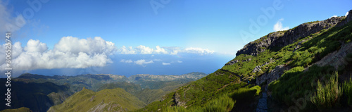 Wide panoramic view of Madeira island high in mountains. Cliff and mountains with blue skies and clouds in background