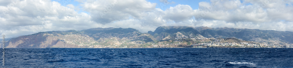 Wide panoramic view of Madeira island. High buildings and town on an island with blue skies and clouds in background