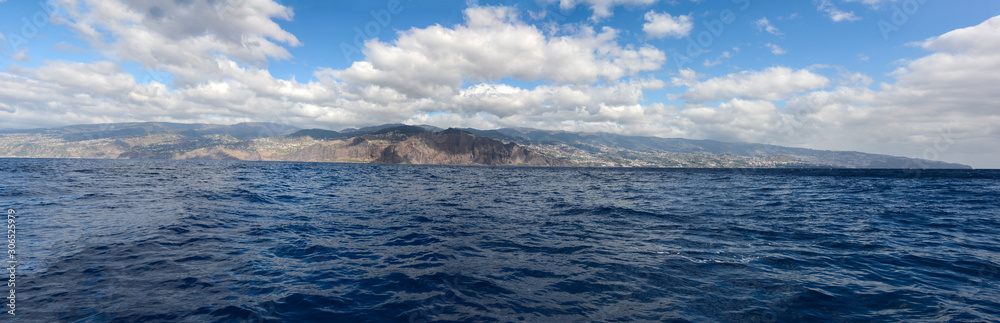 Wide panoramic view of Madeira island. High buildings and town on an island with blue skies and clouds in background Wide panoramic view of Madeira island. High buildings and town on an island with blue skies and clouds in background
