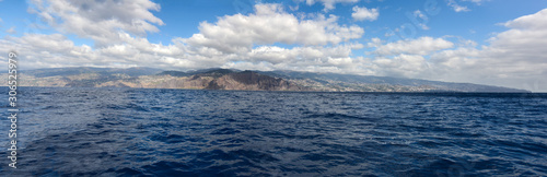 Wide panoramic view of Madeira island. High buildings and town on an island with blue skies and clouds in background