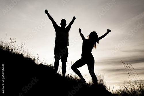 Siluetas de una pareja (chico y chica) con las manos en alto mirándo hacia delante y de perfil en una puesta de sol mientras hacían deporte (trekking) por el monte (montaña) en Andalucia. en color