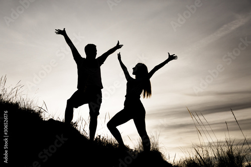 Siluetas de una pareja (chico y chica) con las manos en alto mirándose y de perfil en una puesta de sol mientras hacían deporte (trekking) por el monte (montaña) en Andalucia. en color
