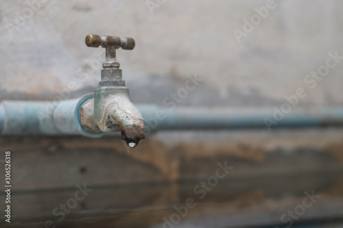 Water that is dripping from the vintage old brass tap that connects to the pvc pipe with the cement wall background.