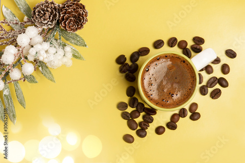 Beautiful christmas decoration. Christmas tree branch with pine cone. Fresh arromatic black coffee cup, and coffee beans, on the yellow background. photo