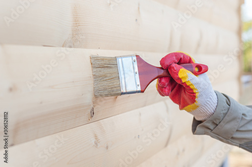 Man paints a wooden house with paint and a brush on the street.