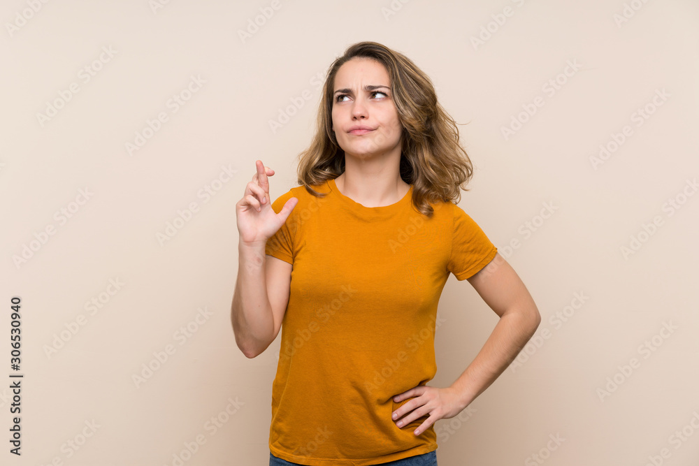 Young blonde girl over isolated background with fingers crossing and wishing the best