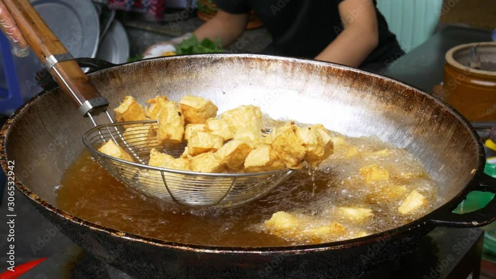 Deep fried tofu cooking in big pan or wok filled with frying oil. Street food stall in Vietnam
