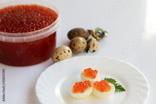 Red caviar. Sandwich with red caviar and quail egg. White background, white plate. Big jar with red caviar. Copy space