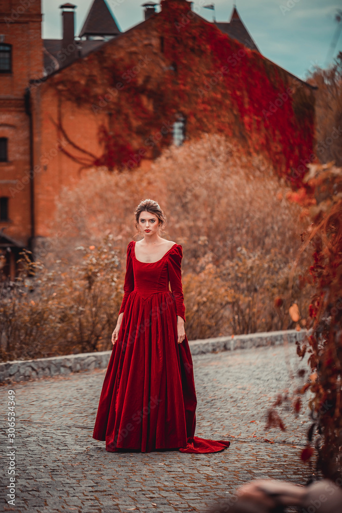 Beautiful girl in a burgundy red dress walking near old castle on a background of autumn grape leaves in the park, October. Radomyshl Beautiful girl in a burgundy red dress walking near old castle on a background of autumn grape leaves in the park, October. Radomyshl