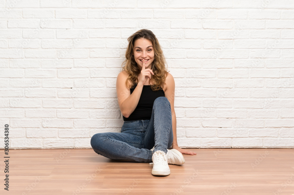 Young blonde woman sitting on the floor doing silence gesture Young blonde woman sitting on the floor doing silence gesture