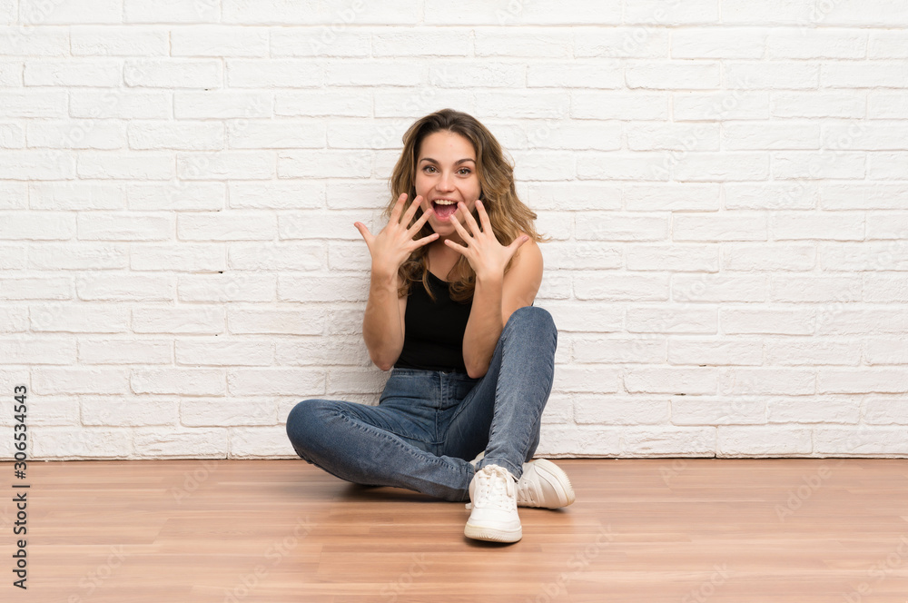 Young blonde woman sitting on the floor with surprise facial expression Young blonde woman sitting on the floor with surprise facial expression