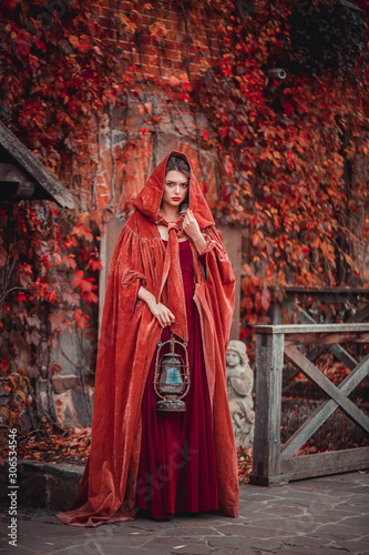 Beautiful girl in a burgundy coat and red dress on the background of the castle in the park, October © popovatetiana