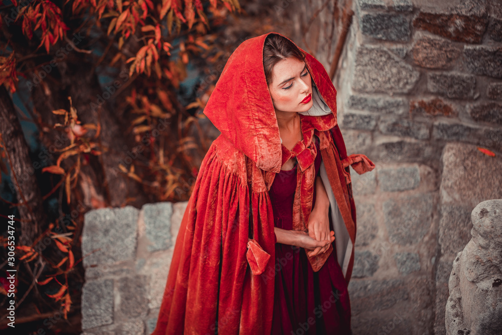 Naklejka premium Beautiful girl in a burgundy coat and red dress on a background of autumn grape leaves in the park, October