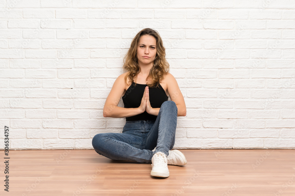 Young blonde woman sitting on the floor pleading Young blonde woman sitting on the floor pleading