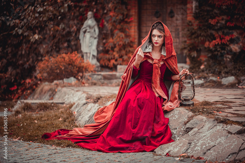 Beautiful girl in a burgundy coat and red dress sitting on the background of the castle in the park, October