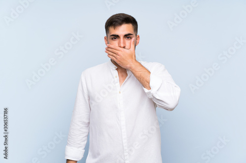 Handsome man with beard over isolated blue background covering mouth with hands