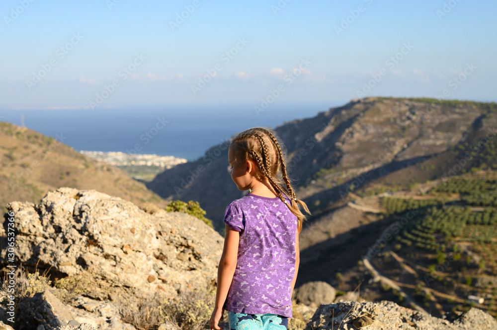A little girl admires the seascape. Family with kids hiking in Greece mountains. Beautiful landscape with hills, sea and sky with low clouds. Outdoor activity in the nature for parents and children