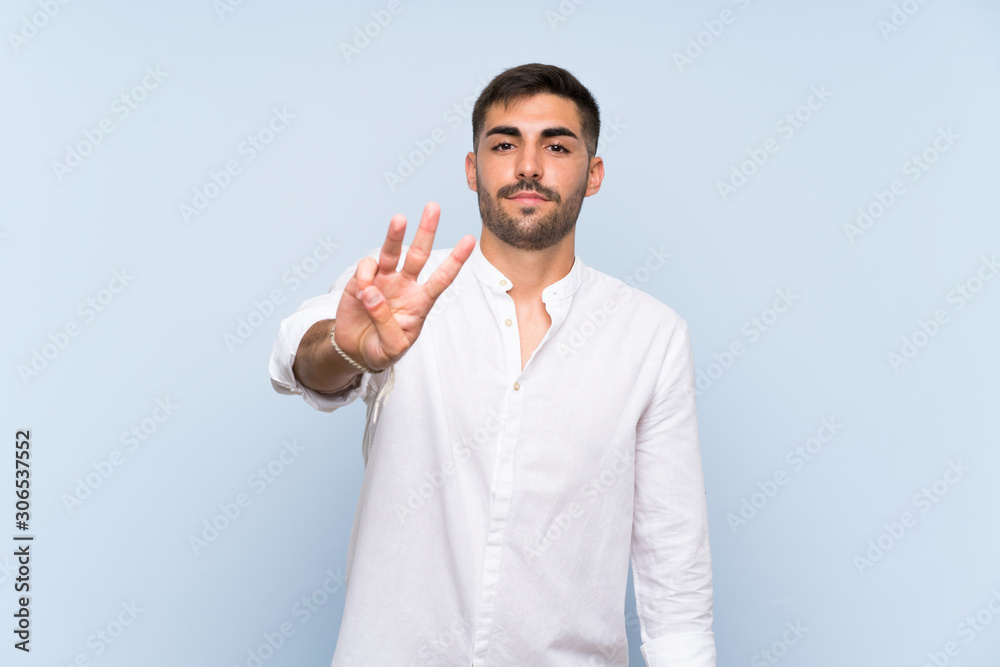 Handsome man with beard over isolated blue background happy and counting three with fingers Handsome man with beard over isolated blue background happy and counting three with fingers