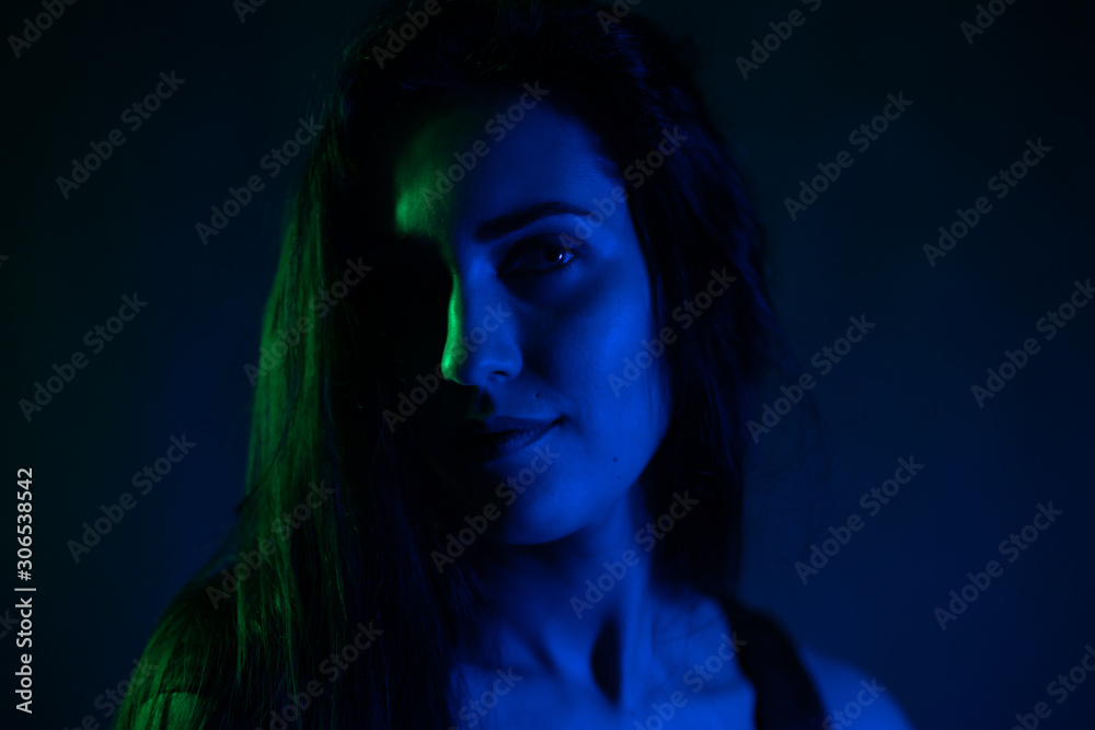 Studio portrait of a girl in the light of blue and green neon lights. on a black background.