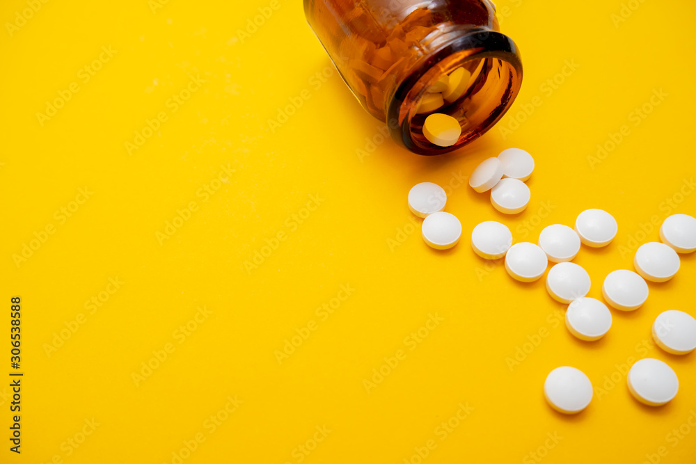 Many white tablets and brown glass container close up on yellow background with copy space, autumn and winter viral disease , infection Many white tablets and brown glass container close up on yellow background with copy space, autumn and winter viral disease , infection
