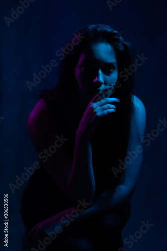 studio portrait of a beautiful girl in the light of blue and magenta neon lights sits on a chair. on a black background.