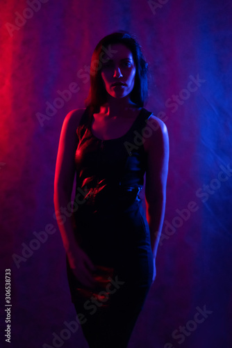 Studio portrait of a beautiful girl in a black dress. in the light of red and blue lamps.