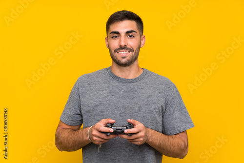 Young handsome man playing with a video game controller over isolated yellow background © luismolinero