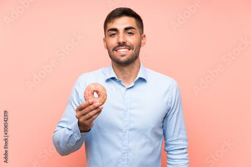 Young man holding a donut over isolated pink background