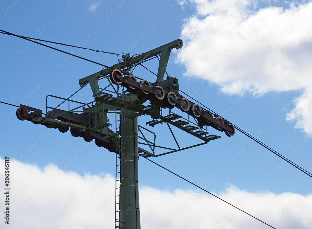 a modern steel cable car pylon with wheels and wires against a blue cloudy sky