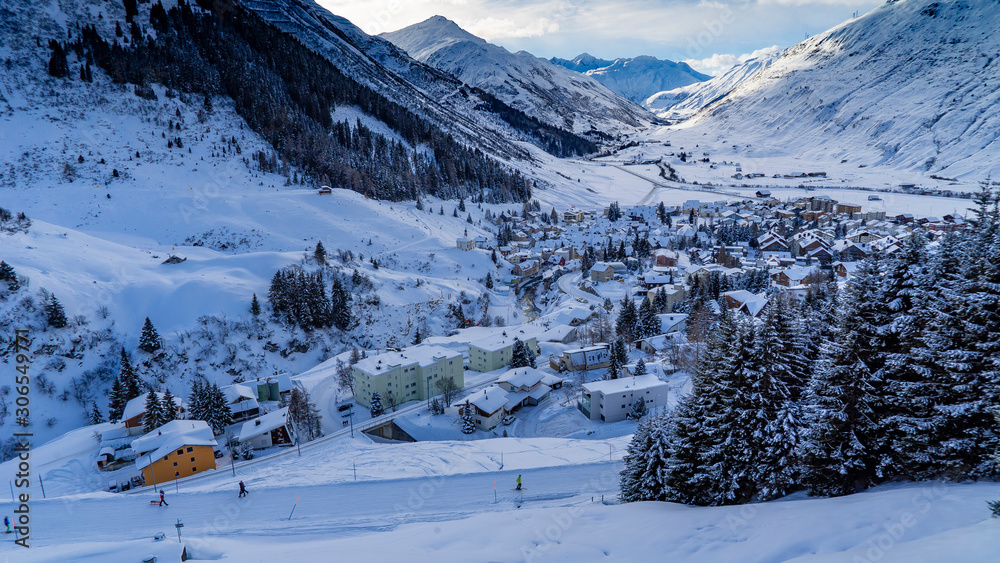 Village enneigé avec des sapins dans une vallée alpine en Suisse avec des montagnes au loin et un ciel nuageux
