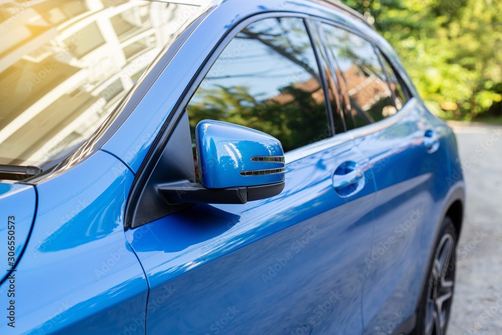 Car Door mirror, side mirror or wing mirror of blue folded when parking on roadside.    Lighting glowing on blue luxury car. Close up and selective focus.