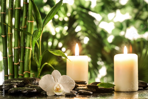 Grean bamboo leaves, white orchid, towel and candles over zen stones on tropical leaves background