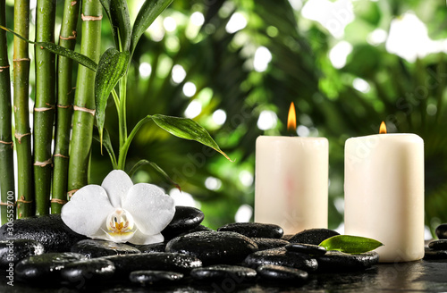 Fototapeta Naklejka Na Ścianę i Meble -  Grean bamboo leaves, white orchid, towel and candles over zen stones on tropical leaves background