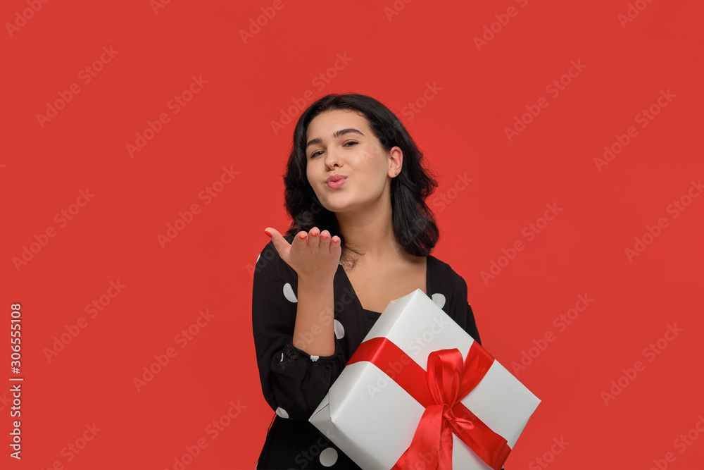 Brunette woman in a black dress smiling holding Christmas giftbox of white color with red ribbon. Brunette woman in a black dress smiling holding Christmas giftbox of white color with red ribbon.